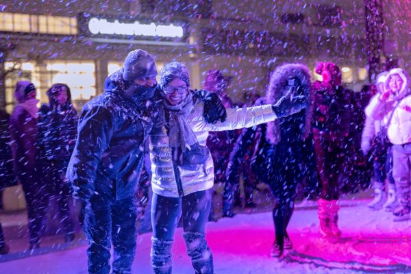 A crowd skating at an outdoor rink at night while it's snowing