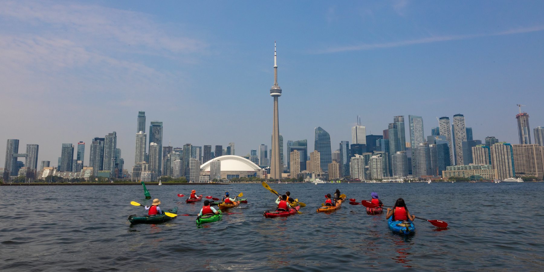 A group of children on kayaks on Lake Ontario with the Toronto skyline in the background