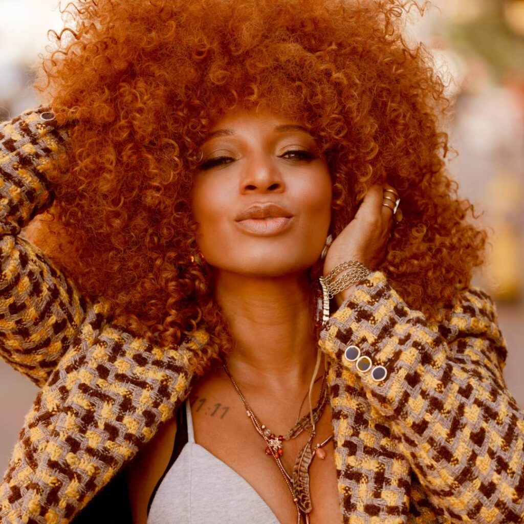 A woman posing for the camera wearing a patterned jacket and holding her red hair
