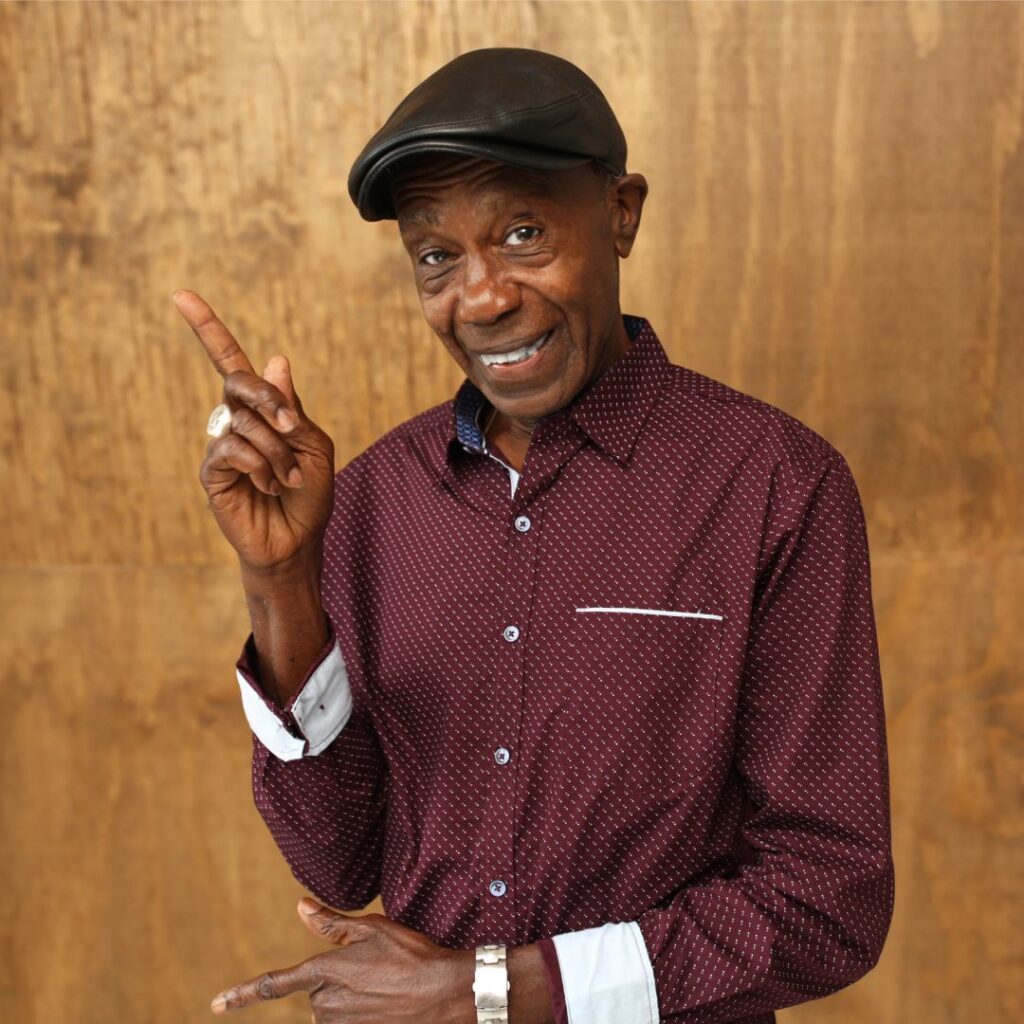 A  man wearing a red shirt and dark hat posing for camera