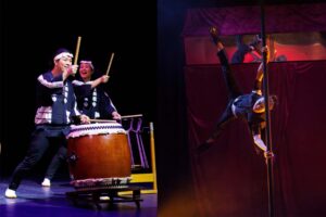 Drummers performs with a taiko drum next to someone doing acrobatics with a pole.