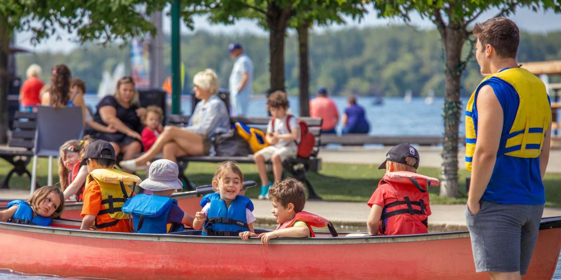 A canoe instructor with a group of kids on a lake outside.