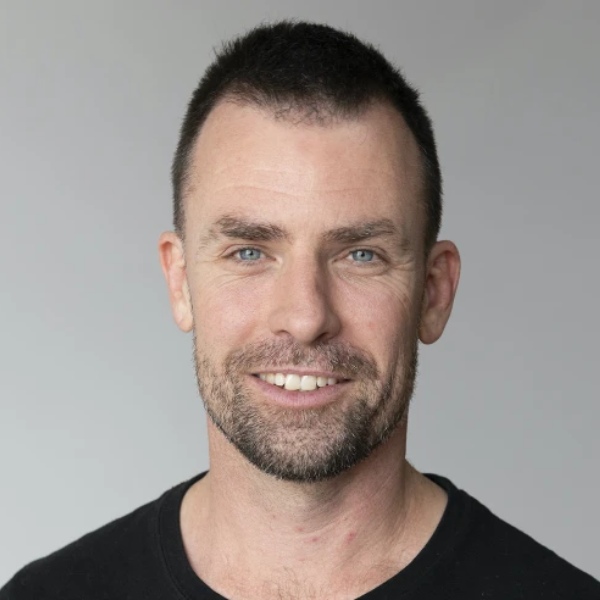 A headshot of a man smiling against a grey background