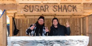 Two men standing outside in a sugar shack posing for the camera