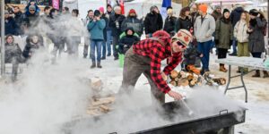 A man wearing a red and black plaid shirt doing a sugar related activity outdoors in front of a crowd
