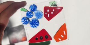 A close-up shot of a hand holding a colourful glass fused piece