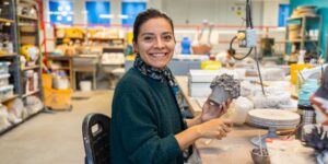 An artist smiling and posing with a ceramic cup piece in studio