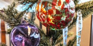 Holiday glass ornament in bright red and purple colours hanging on a tree