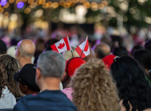A crowd of people sitting in seats holding small Canadian flags