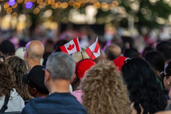 A crowd of people sitting in seats holding small Canadian flags