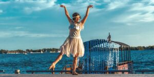 A woman in 1920s attire dancing and posing in front of a waterfront outdoors