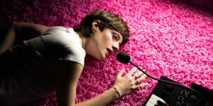 A person lying down on a pink floor holding a microphone
