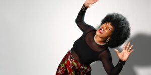 A woman wearing a black shirt with her hands up and eyes closed posing