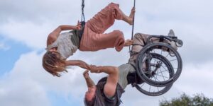 Two people suspended in air holding onto each other, one in a wheelchair
