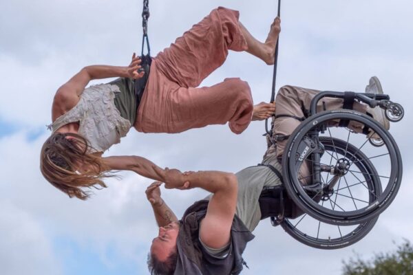 Two people suspended in air holding onto each other, one in a wheelchair