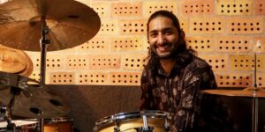 A musician smiling for the camera sitting with drums.