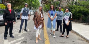 A group of six musicians posing outdoors on a road