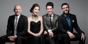A group of four musicians dressed in black posing while sitting down