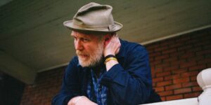 A man wearing a blazer and hat standing on a balcony holding glasses