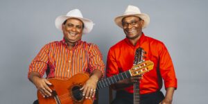 Two musicians wearing hats and bright red shirts posing with guitars.