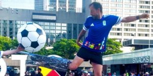 A circus performer posing as a referee on stilts kicking a soccer ball