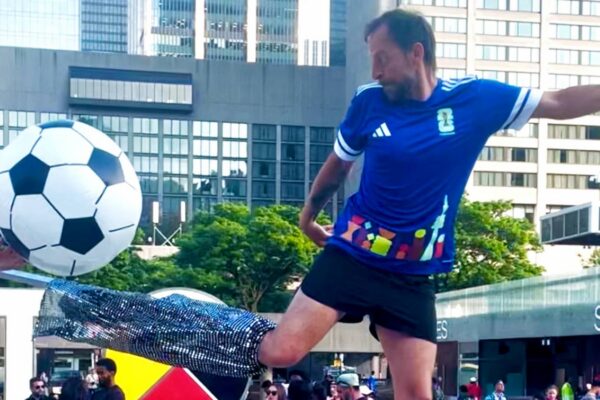 A circus performer posing as a referee on stilts kicking a soccer ball