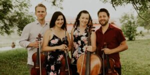 A group of four musicians posing with their instruments outdoors.