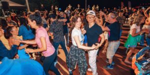 A group of people dancing outdoors by the lake at night