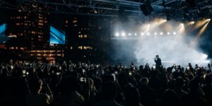 An outdoor concert with a performer on stage in front of a crowd at night