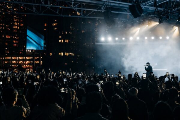 An outdoor concert with a performer on stage in front of a crowd at night