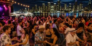 A crowd dancing outside by a city skyline at night