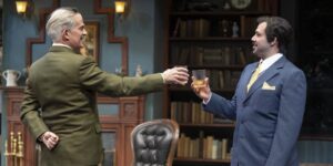 Two actors on stage holding glasses.
