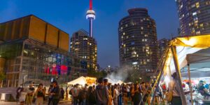 A nighttime shot of a crowd at an outdoor food market with the CN tower in the background