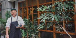 A chef posing in front of a restaurant holding a dish.