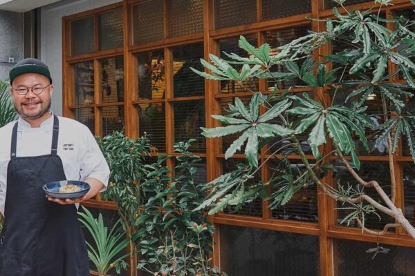 A chef posing in front of a restaurant holding a dish.