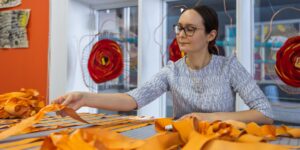 An artist holding a bright orange textile material in a studio