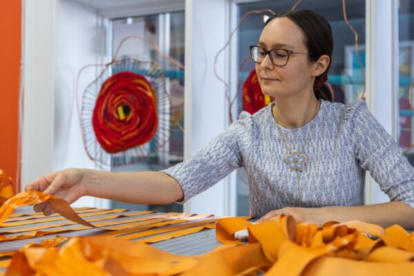 An artist holding a bright orange textile material in a studio