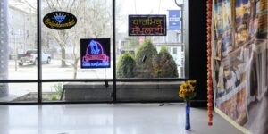 An art exhibition with a blue vase and flowers sitting on the floor against windows.