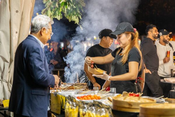 A market vendor serving skewers to a customer outside at night